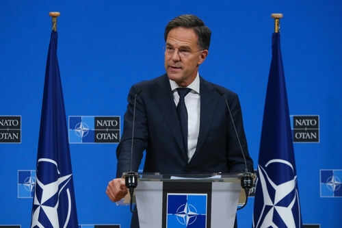 Man speaking at podium with NATO flags behind him