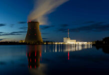 Cooling tower of a power plant at night beside a calm river