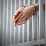 handcuffed hands resting through prison bars