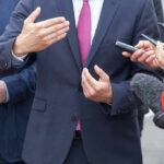 Rental Truck? Texas Senate Ad Backfires Businessperson in suit speaking to reporters with microphones