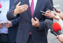 Businessperson in suit speaking to reporters with microphones