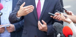 Businessperson in suit speaking to reporters with microphones