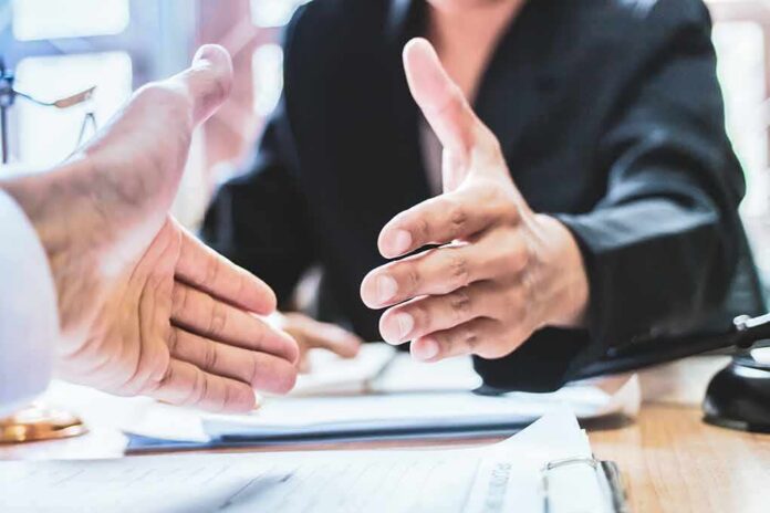 shutterstock_1116829721 Two people extending hands for a handshake across a desk
