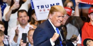 man in suit raising fists at a rally podium