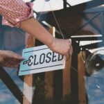Hands hanging a closed sign on a glass door