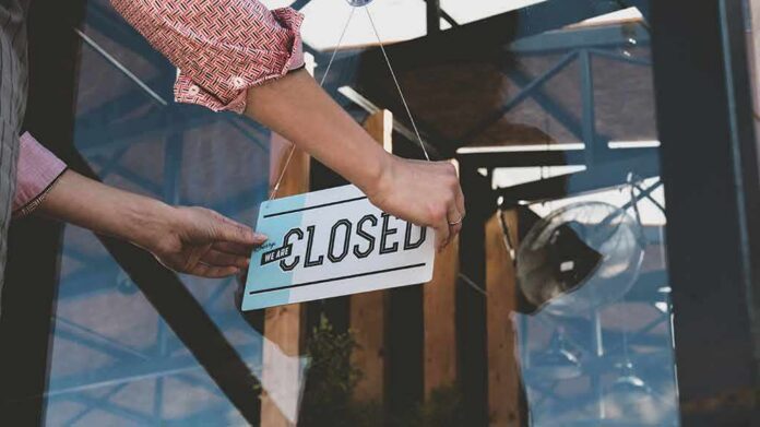Hands hanging a closed sign on a glass door