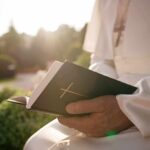 Person in white robe holding a Bible outdoors