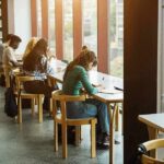 Students studying at long tables by large library windows