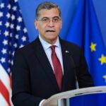 Aides Skimmed Cash—Becerra Blindsided? Government official speaking at a podium with flags in the background