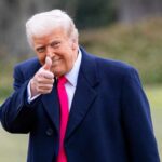 Trump’s Swag Room Raises Eyebrows A man in a dark coat and pink tie giving a thumbs up outdoors