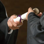 Two individuals exchanging a diploma during a graduation ceremony
