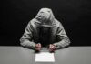 Person in gray hoodie writing while handcuffed at a table