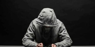 Person in gray hoodie writing while handcuffed at a table