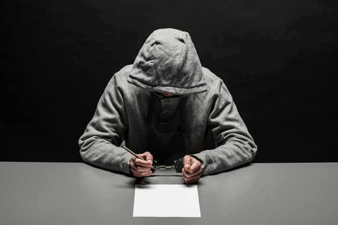 Person in gray hoodie writing while handcuffed at a table