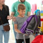 Boy choosing a purple backpack in a store with adults nearby