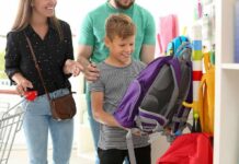Boy choosing a purple backpack in a store with adults nearby