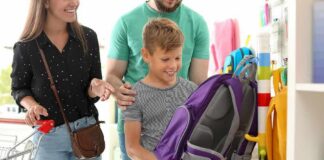 Boy choosing a purple backpack in a store with adults nearby