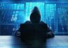 Water Systems Breached — Who’s Behind It? Hooded figure using a laptop in front of glowing code