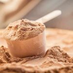 Whey Boom Hijacks Dairy — Farmers Squeezed Scoop of chocolate protein powder in a measuring cup