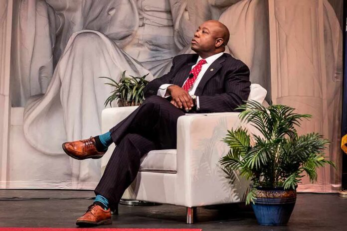 Man in suit seated in white armchair on stage