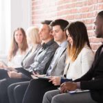 Shrinking Workforce Warps Unemployment Hype Job candidates seated in a row against a brick wall