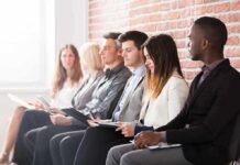 Shrinking Workforce Warps Unemployment Hype Job candidates seated in a row against a brick wall