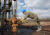 Libya Valve Mutiny Risks Price Shock Worker in blue hard hat operating rusty oil pump equipment outdoors