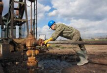 Libya Valve Mutiny Risks Price Shock Worker in blue hard hat operating rusty oil pump equipment outdoors