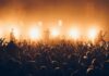 Rock band performing on stage with bright backlights and cheering crowd