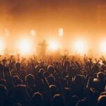 Rock band performing on stage with bright backlights and cheering crowd