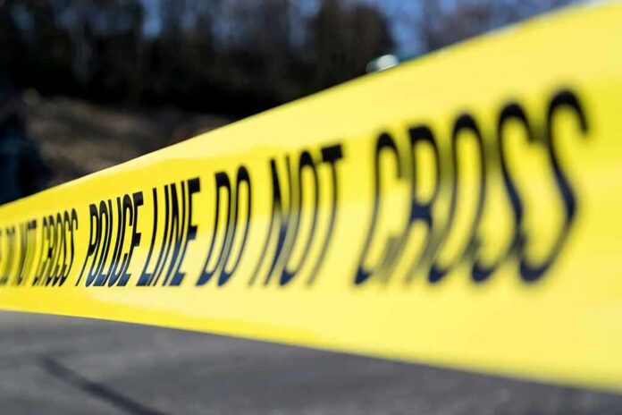 shutterstock_1347630851 Yellow police tape stretched across an outdoor scene