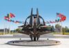 NATO emblem sculpture surrounded by member flags