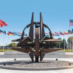 NATO emblem sculpture surrounded by member flags