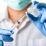 Healthcare worker drawing vaccine from vial with syringe