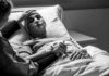 Patient in hospital bed with nasal oxygen held by visitor