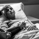 Bishops Warn: Door To Euthanasia Cracks Open Patient in hospital bed with nasal oxygen held by visitor