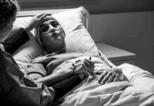 Patient in hospital bed with nasal oxygen held by visitor