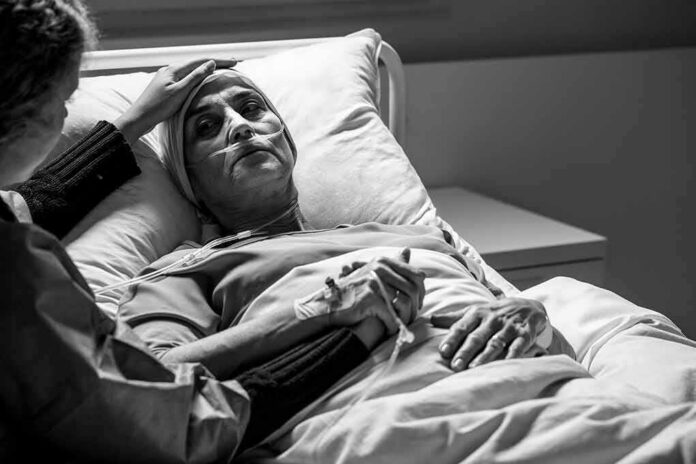 Patient in hospital bed with nasal oxygen held by visitor