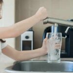 Girl filling a glass with water at a kitchen sink