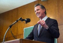 Gavin Newsom speaking at a podium with microphones
