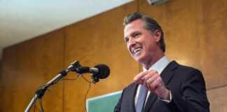 Gavin Newsom speaking at a podium with microphones