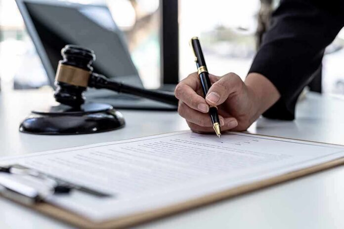 shutterstock_2103308165 Hand signing legal document beside gavel and laptop