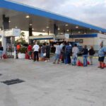 People waiting with red fuel cans at a gas station
