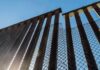 Border Whiplash: Tijuana Beds Go Empty Steel border fence with chain-link mesh under blue sky