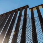 Steel border fence with chain-link mesh under blue sky