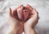 Adult hands cradling newborn baby feet
