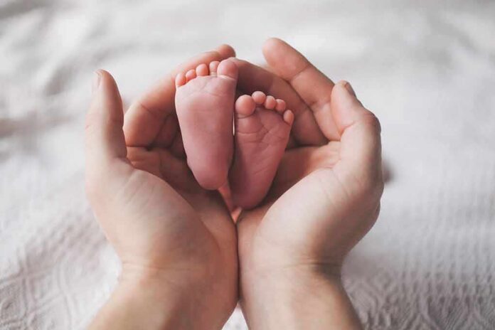shutterstock_523810459 Adult hands cradling newborn baby feet