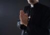 Eucharist Drama Erupts In Manhattan Clergyman in black robe praying with hands together