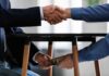 Bribe Vibes? ‘Elementary School’ Politics Two people shake hands while exchanging cash under a table