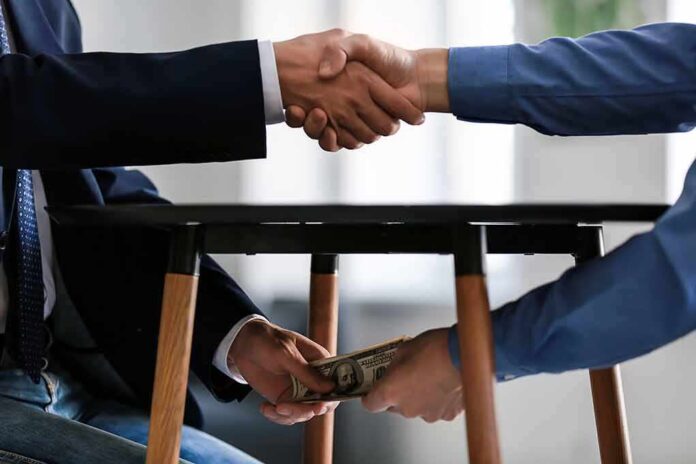 shutterstock_1225177960 Two people shake hands while exchanging cash under a table